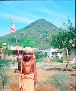 1982 (approximately). His Divine Holiness Paramahamsa Nithyananda cognized Himself as a Sanyasi (Monk as per Sanatana Hindu Dharma or Hinduism) from the very beginning. This picture is taken at approximately age 4, when He started wandering in Tiruvannamalai, His birthplace, and virtually lived in Pavazha Kundru – a historic spot atop the sacred Arunachala Hill where Devi (Cosmic Mother) realised herself as Ardhanareeshwara – the Hindu God who is the perfect synthesis of the male and female energies. Here, He is seen near Draupadi Amman temple, near His yoga Guru – Ragupathi Yogi’s house in Tiruvannamalai, South India. 