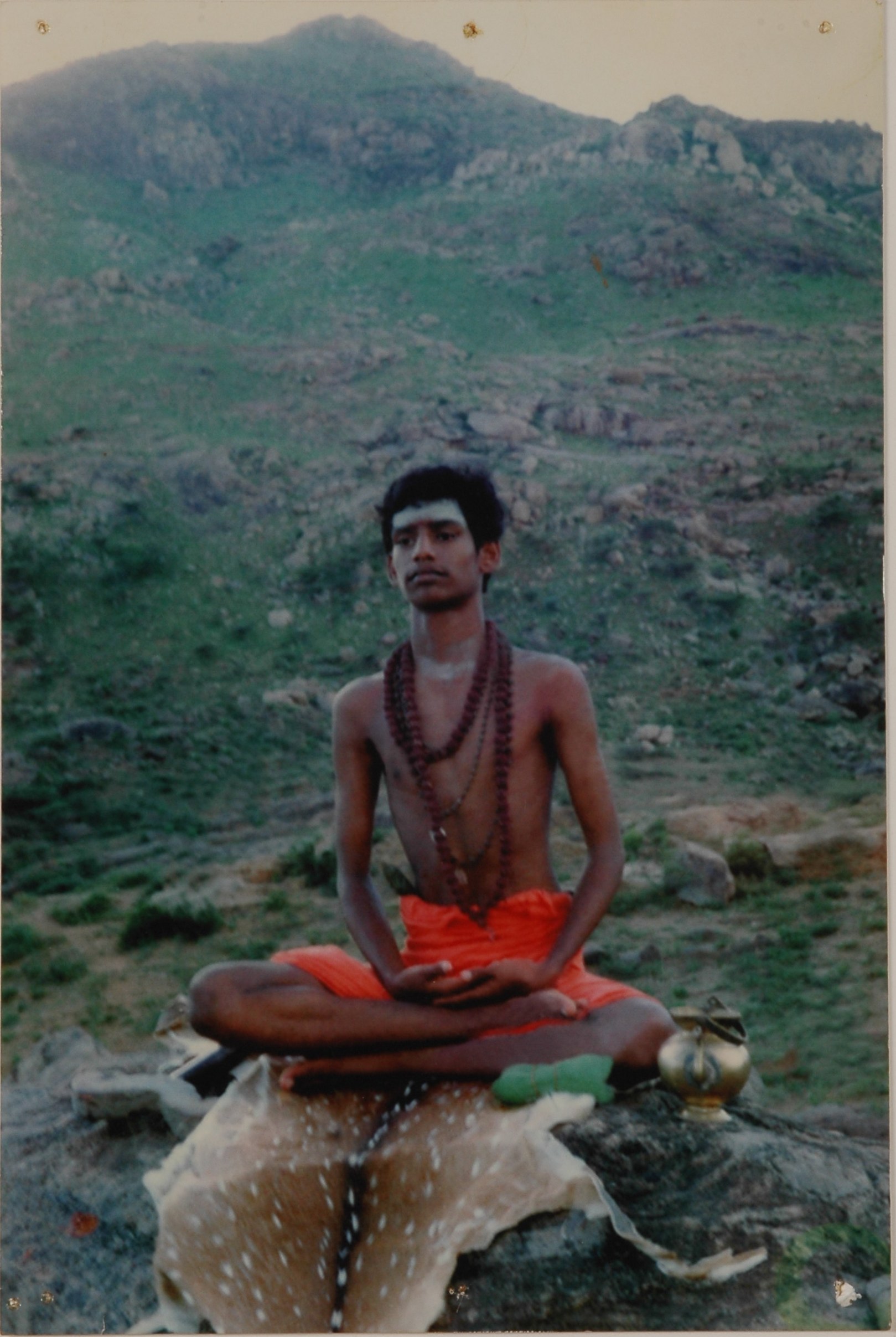 In this picture Paramahamsa Nithyananda is seen seated on The Sadashiva Shila – His enlightenment experience rock - in Pavazha Kundru where he had his enlightenment experience. He sits with the very same danda (wooden staff) and kamandalu (water pot) given to him by Matha Vibhutananda Puri, or Mataji Kuppammal